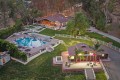 Aerial view of a luxury estate with a rectangular pool, lounge chairs, umbrellas, and a clubhouse surrounded by lawns and trees, at dusk light.”,