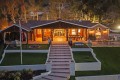 Evening view of a brick house with a large illuminated covered patio, outdoor seating, and a central stairway to a manicured lawn.