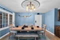 Rustic dining room with a weathered wooden table, bench, and chairs, blue walls, a longhorn skull wall art, and a brass chandelier.