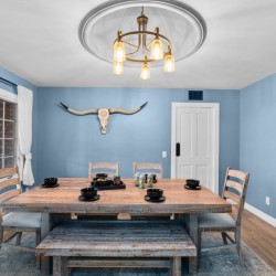 Rustic dining room with a weathered wooden table, bench, and chairs, blue walls, a longhorn skull wall art, and a brass chandelier.