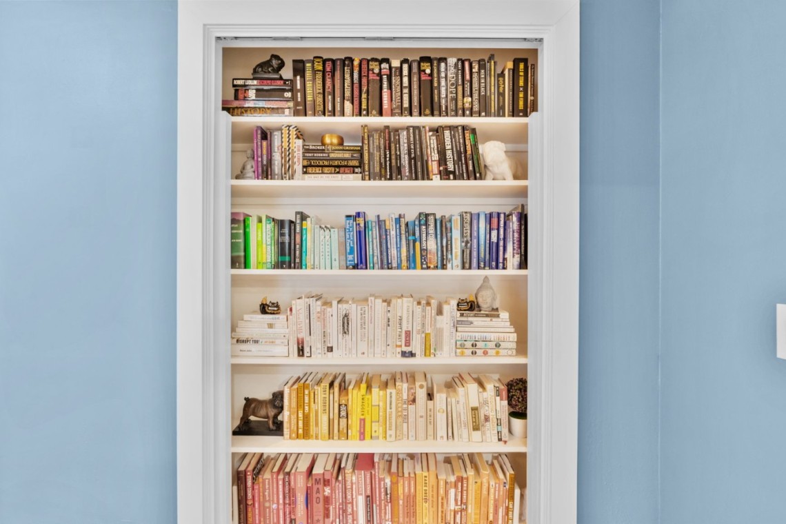 White built-in bookshelf inside a doorway, five shelves of colorful books against blue walls.