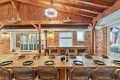 Rustic brick dining room with a long wooden table set for a meal, wine bottles in the center and woven chairs around it.