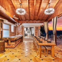 Outdoor covered patio with brick walls and a long dining table set for 12, facing a sunset view on the horizon.