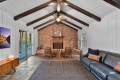 Cozy living room with a brick fireplace, vaulted ceiling with exposed dark wood beams, and a sliding glass door outside.