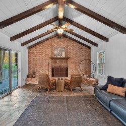 Cozy living room with a brick fireplace, vaulted ceiling with exposed dark wood beams, and a sliding glass door outside.