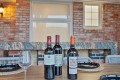 Three wine bottles centered on a wooden table with place settings against a brick-walled outdoor patio backdrop.