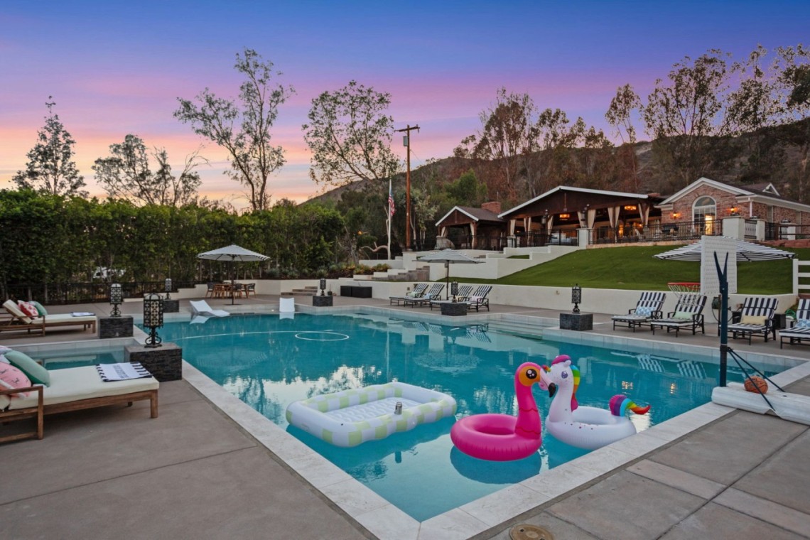 Poolside resort scene at sunset with lounge chairs, umbrellas, and inflatable floats in the waterhttps://? (note: no URL)