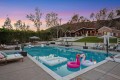 Poolside resort scene at sunset with lounge chairs, umbrellas, and inflatable floats in the waterhttps://? (note: no URL)