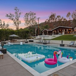 Poolside resort scene at sunset with lounge chairs, umbrellas, and inflatable floats in the waterhttps://? (note: no URL)
