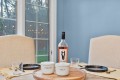 Dining table setup with a wine bottle, salt and pepper bowls, and empty glasses against a blue wall and beige chairs.