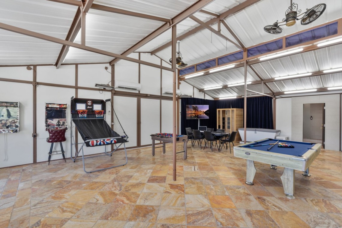Indoor games room with pool table, foosball, arcade basketball game, and a seating area with a TV in the back corner.