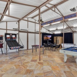 Indoor games room with pool table, foosball, arcade basketball game, and a seating area with a TV in the back corner.