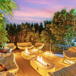 Cozy rooftop patio with cream cushioned seating around two fire pits at dusk, surrounded by greenery and lanterns