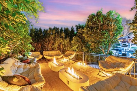 Cozy rooftop patio with cream cushioned seating around two fire pits at dusk, surrounded by greenery and lanterns
