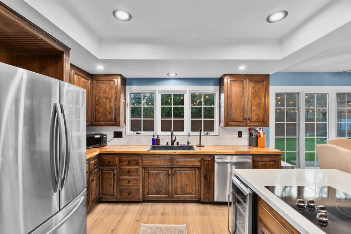 Kitchen with dark wood cabinets, stainless steel refrigerator, and a central island stove under recessed lighting. Windows overlook a backyard.