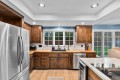 Kitchen with dark wood cabinets, stainless steel refrigerator, and a central island stove under recessed lighting. Windows overlook a backyard.