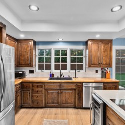 Kitchen with dark wood cabinets, stainless steel refrigerator, and a central island stove under recessed lighting. Windows overlook a backyard.