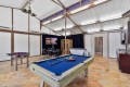 Bright game room with a blue pool table in the foreground, foosball, a dining table, and a TV area in back.