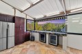 Modern kitchen with a stainless steel French-door fridge, dark wood cabinets, and marble countertop, overlooking a sunset hillside from a large window.