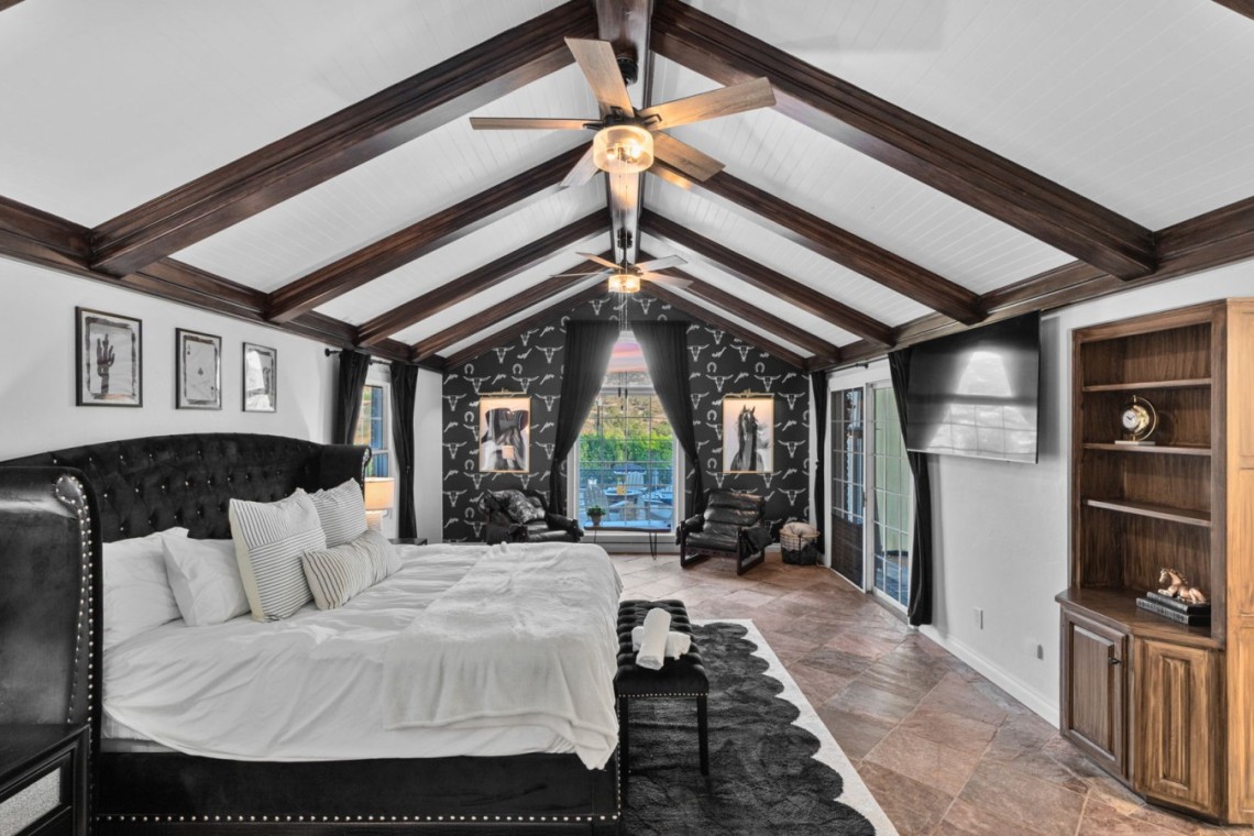 Luxurious loft bedroom with a black tufted bed, white bedding, and dark wood beam ceiling.