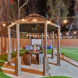 Nighttime backyard gazebo with string lights, a round table, wicker stools, and a Jenga tower on the table.