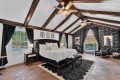 Luxurious bedroom with vaulted white ceiling, dark wood beams, and a black tufted bed with matching nightstands.