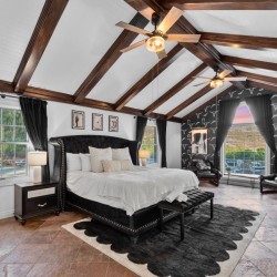 Luxurious bedroom with vaulted white ceiling, dark wood beams, and a black tufted bed with matching nightstands.