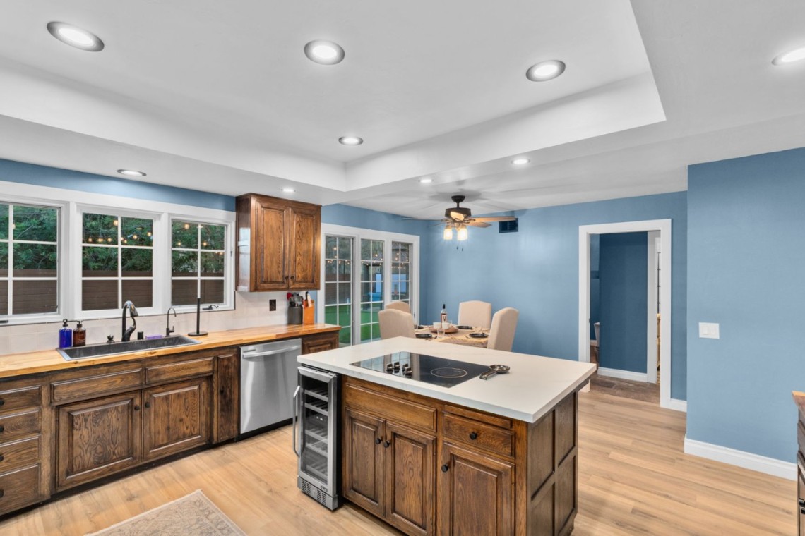 Bright kitchen with blue walls, dark wood cabinets, a central island with a cooktop, and a dining area beyond.