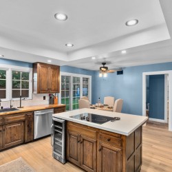Bright kitchen with blue walls, dark wood cabinets, a central island with a cooktop, and a dining area beyond.