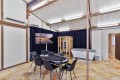 Round poker table with chips and eight chairs in a bright industrial-style room; wall TV on dark curtains, wooden sauna cabinet, and a white spa tub nearby under bright lighting.