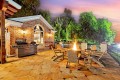 Brick house patio with outdoor grill, burning fire pit, and circular seating around the flames at sunset.