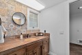 Wood-toned bathroom vanity with brown countertop, oval sink, and a colorful tile backsplash under a round mirror.