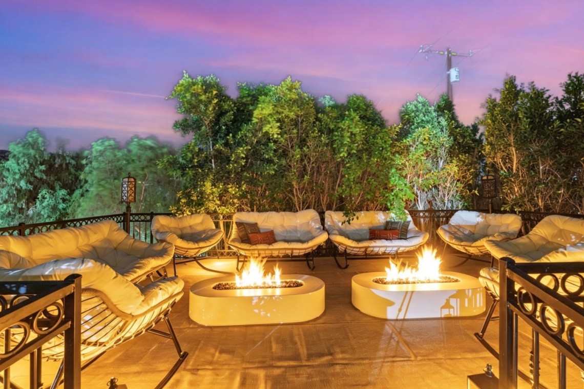 Outdoor lounge area at dusk with cream cushioned chairs surrounding two glowing fire pits on a tiled terrace.