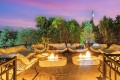 Outdoor lounge area at dusk with cream cushioned chairs surrounding two glowing fire pits on a tiled terrace.
