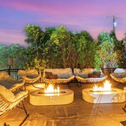 Outdoor lounge area at dusk with cream cushioned chairs surrounding two glowing fire pits on a tiled terrace.
