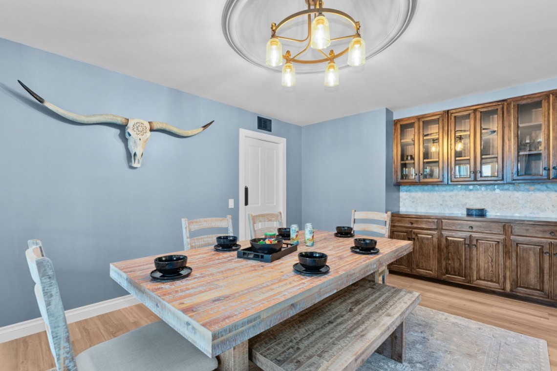 Blue-dk dining room with a rustic wooden table, bench seating, and a longhorn skull wall decor above one wall