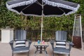 Two blue Adirondack chairs with striped pillows face a small table under a large umbrella; soda cans sit on the table in a backyard patio setting.