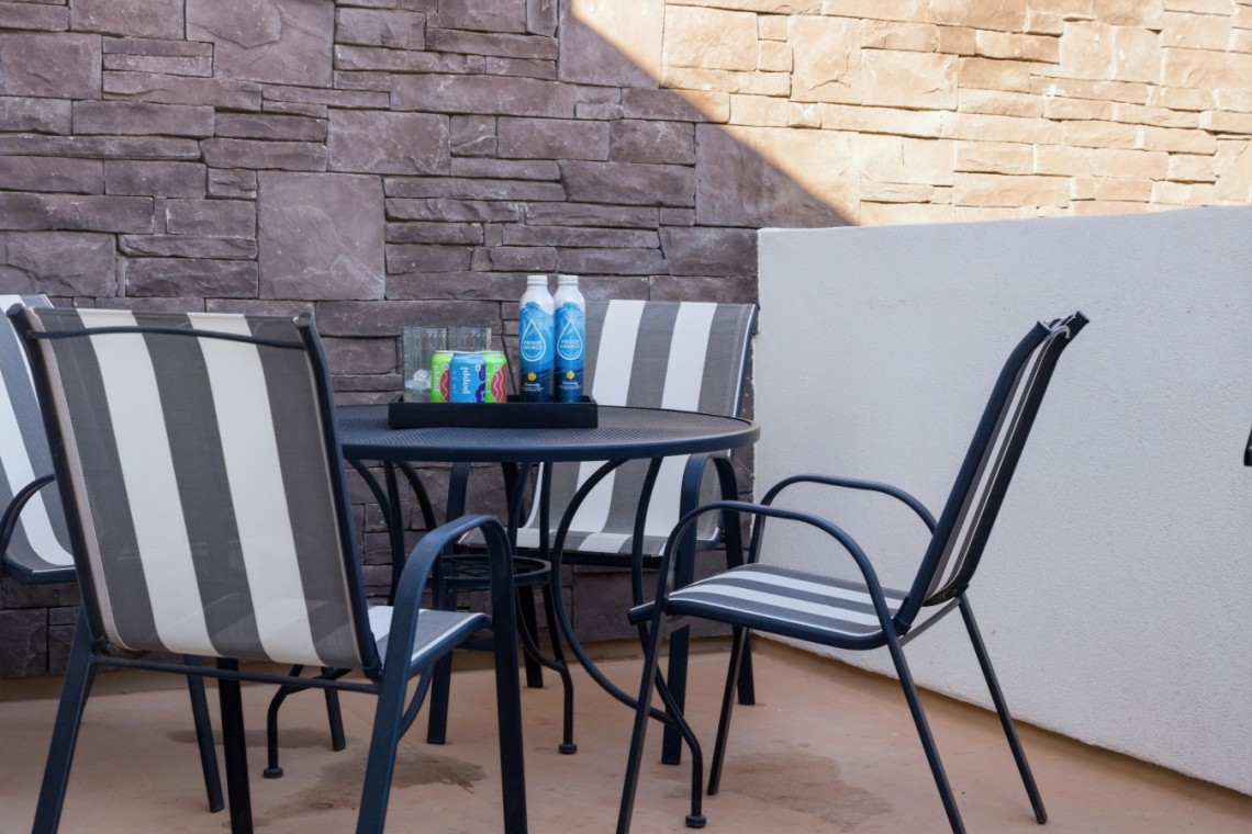 Outdoor patio with a round table, striped chairs, and a tray of drinks (water bottles and soda cans) against a stone wall.