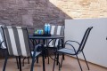 Outdoor patio with a round table, striped chairs, and a tray of drinks (water bottles and soda cans) against a stone wall.