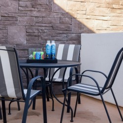Outdoor patio with a round table, striped chairs, and a tray of drinks (water bottles and soda cans) against a stone wall.