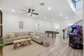 Bright open living room with a beige sectional sofa, woven bench, and neutral rug; foosball table in the back and a kids' NFL arcade machine by the stairs.