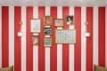 Red and white striped wall with a gallery of gold-framed artworks, including 'It’s all good' and 'How lucky are we,' flanked by brass wall sconces.