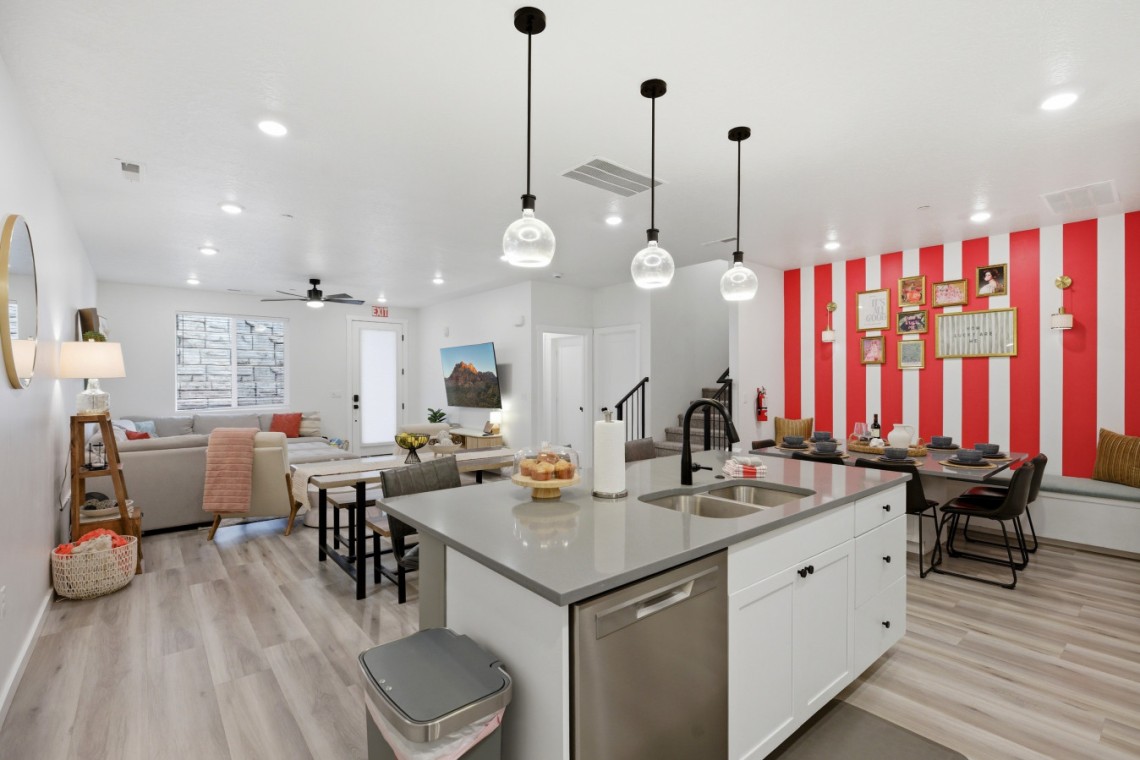 Open-concept living space with a kitchen island, dining area, and a red-and-white striped gallery wall with frames.