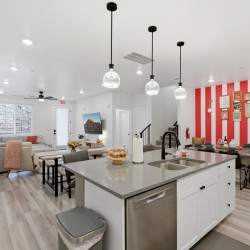 Open-concept living space with a kitchen island, dining area, and a red-and-white striped gallery wall with frames.