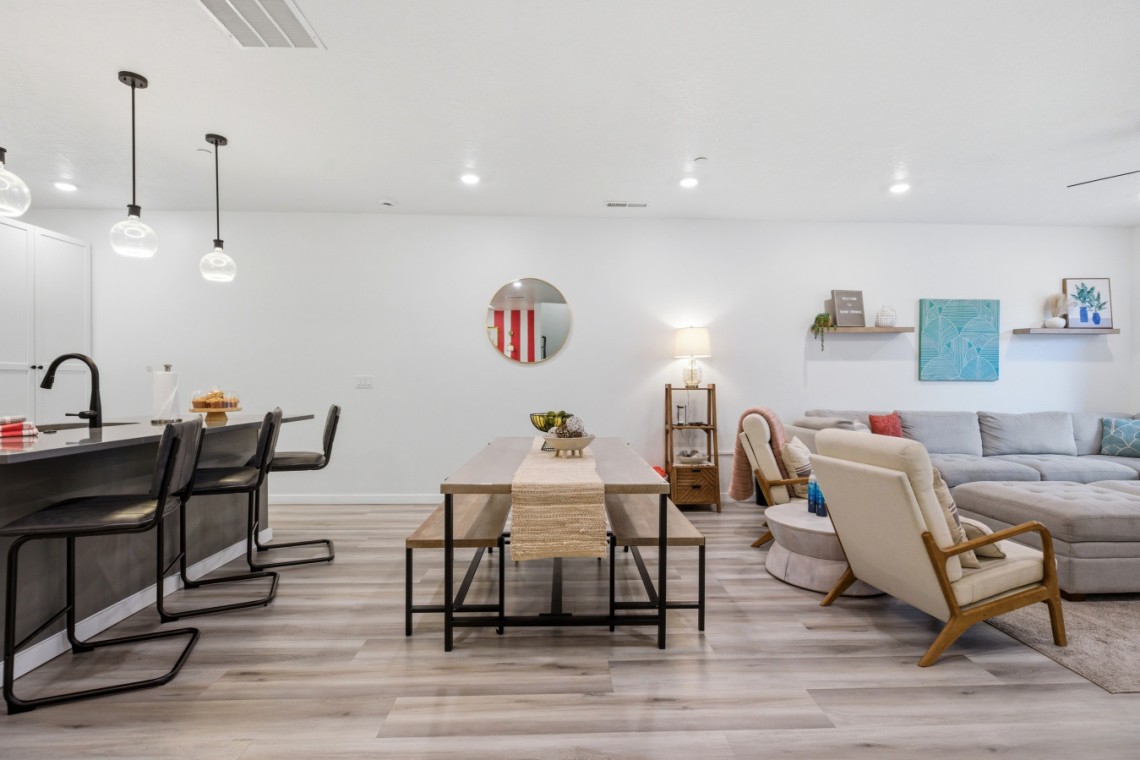 Open-concept living area showing a wooden dining table, bench seating, and a gray sectional sofa in a bright, modern home.