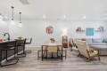 Open-concept living area showing a wooden dining table, bench seating, and a gray sectional sofa in a bright, modern home.