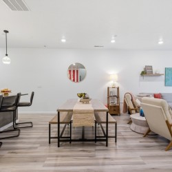 Open-concept living area showing a wooden dining table, bench seating, and a gray sectional sofa in a bright, modern home.