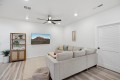 Living room with a light gray sectional sofa, wall-mounted TV, and a wooden shelf against a white wall.