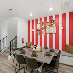Dining area with red and white striped accent wall, gallery wall, built-in bench, and a table set for eight.