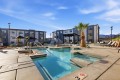 Outdoor pool area at a modern apartment complex with lounge chairs, palm trees, and blue sky.